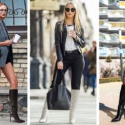 Stylish woman in a gray blazer, black shorts, and knee-high boots walks past a brick wall, holding a coffee.