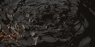 Close-up of dark water surface with ripples and droplets creating circular waves at night.